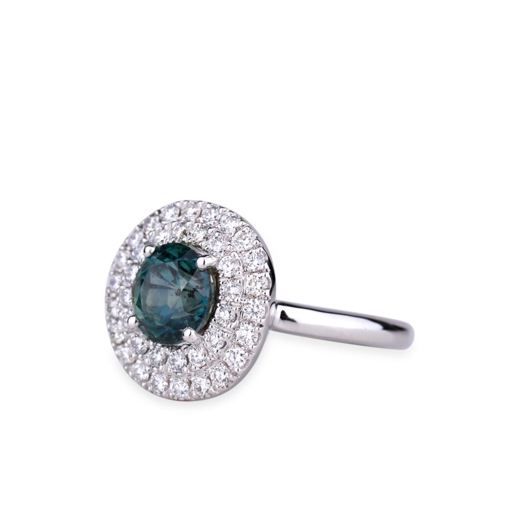 Bague en or blanc sertie d'un saphir vert entouré d’un double halo de diamants.
