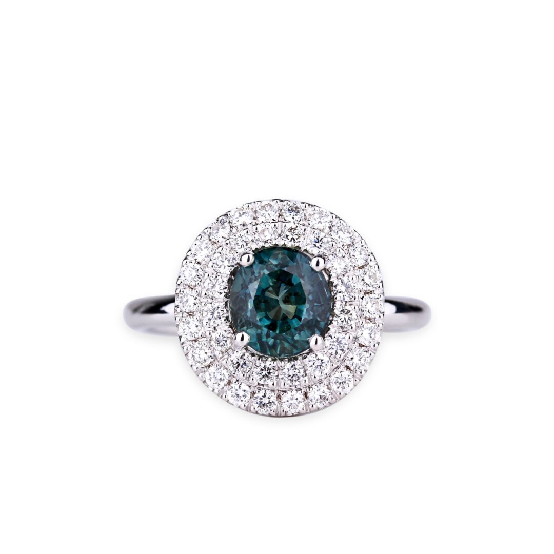 Bague en or blanc sertie d'un saphir vert entouré d’un double halo de diamants.
