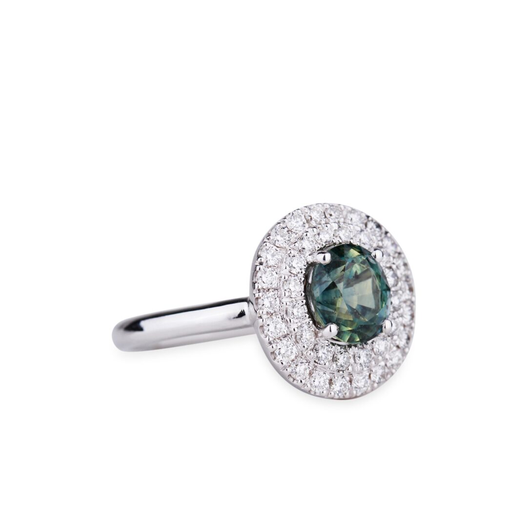 Bague en or blanc sertie d'un saphir vert entouré d’un double halo de diamants.