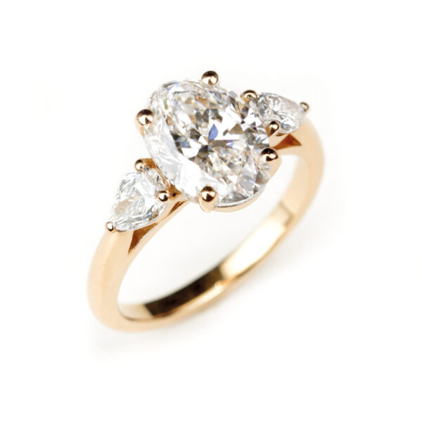 Bague en or rose 18 K avec diamant ovale de 2 carats encadré par deux diamants taille poire.